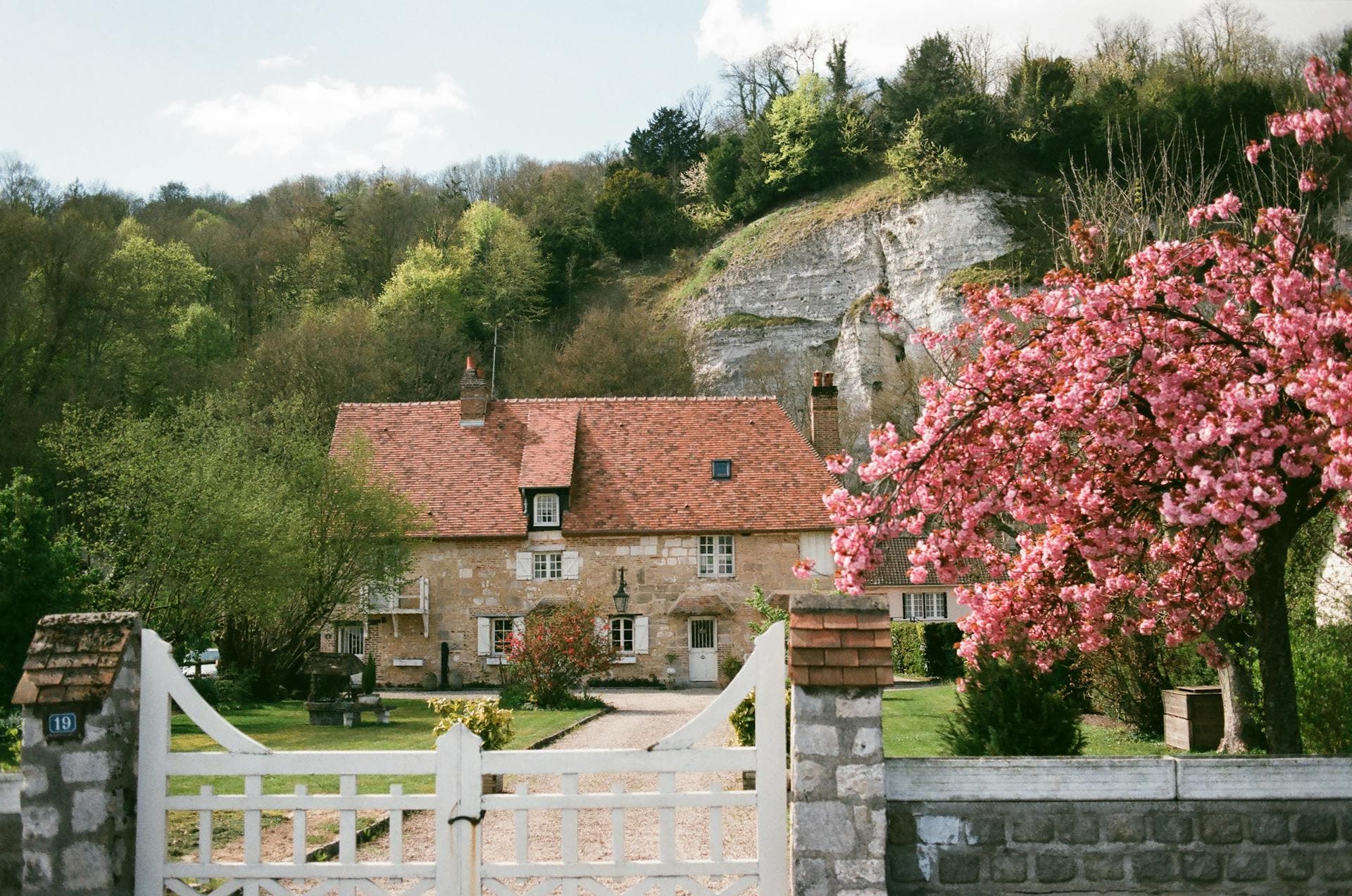 Maison en pierre avec portail blanc et cerisier en fleurs, symbolisant le patrimoine familial à préserver